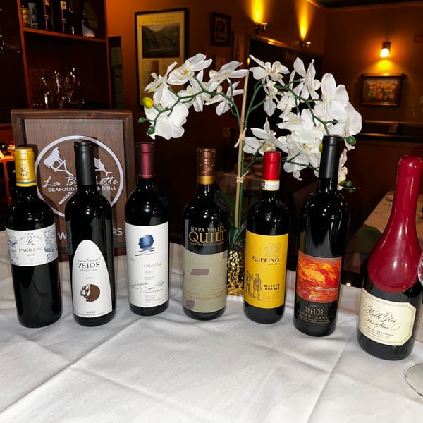 Seven wine bottles, including La Brochette Bistro's, and white orchids on a white tablecloth.