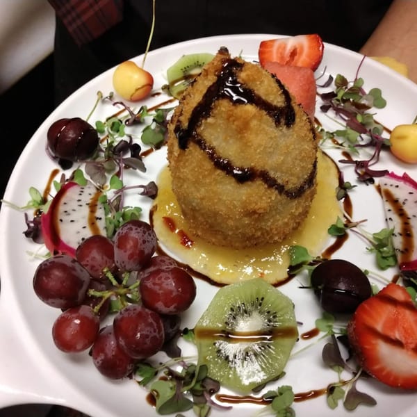 Deep-fried ice cream dessert with fruit, microgreens, and balsamic glaze on a white plate.