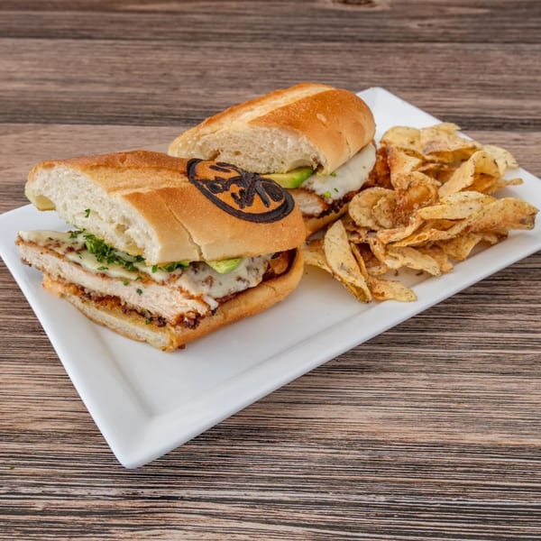 La Brochette Bistro's chicken sandwich with melted cheese, avocado, and chips on a white plate.
