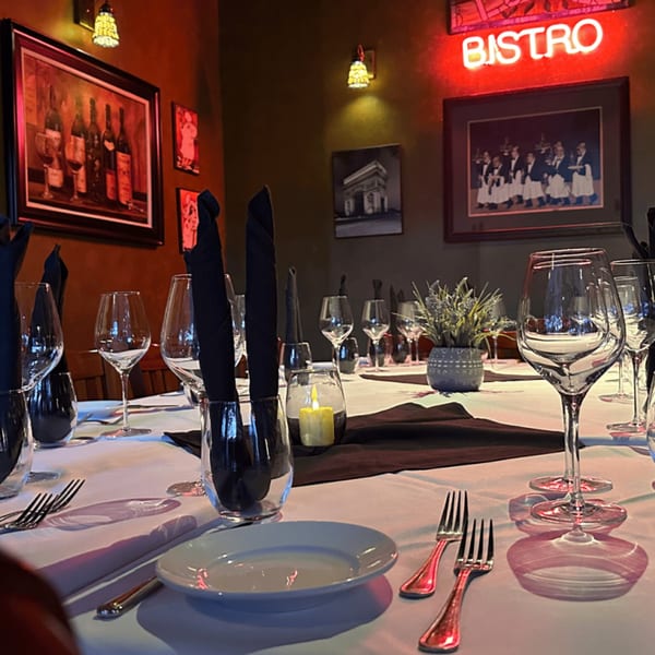 A set table at La Brochette Bistro with wine glasses, black napkins, and a glowing "BISTRO" sign.