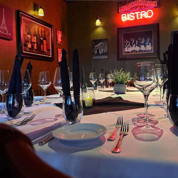 A set table at La Brochette Bistro with wine glasses, black napkins, and a glowing "BISTRO" sign.