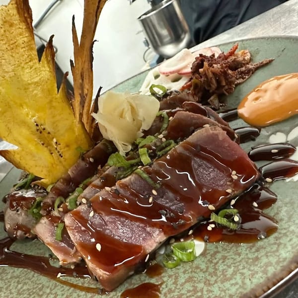 Seared tuna with dark sauce, sesame seeds, green onions, and plantain chips on a green plate.