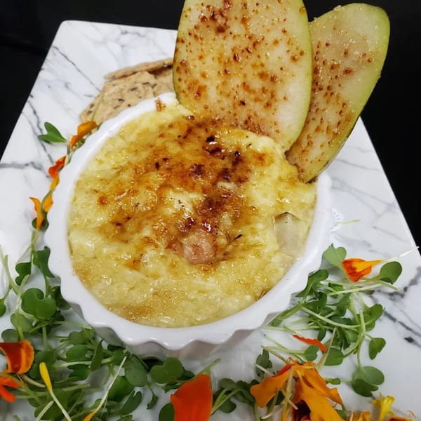 Baked brie with caramelized pears, crackers, and microgreens on a marble plate.