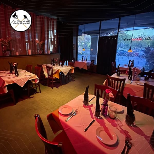 Interior of La Brochette Bistro with set tables, red lighting, and large windows.