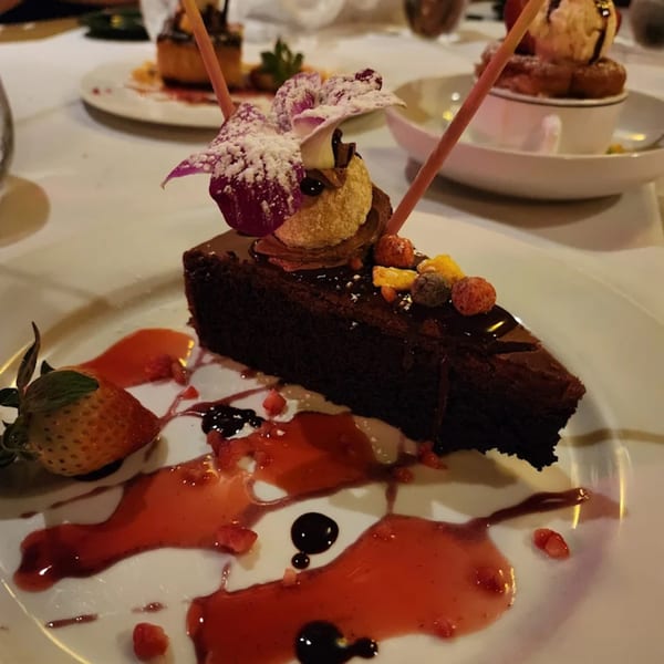 A slice of chocolate cake with strawberry, raspberry, and an orchid on a white plate.