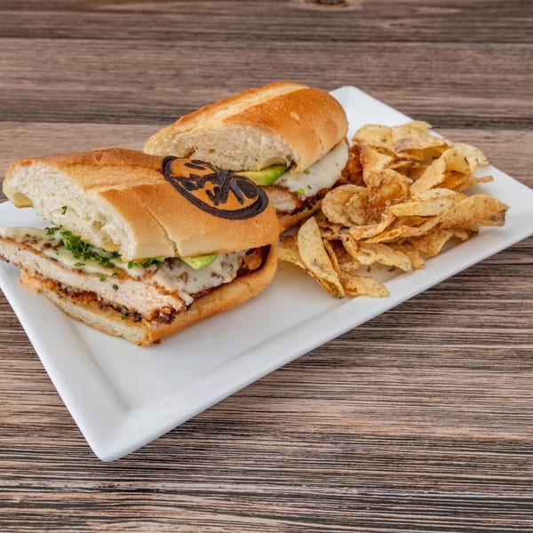 La Brochette Bistro's chicken sandwich with avocado and melted cheese, served with a side of chips.