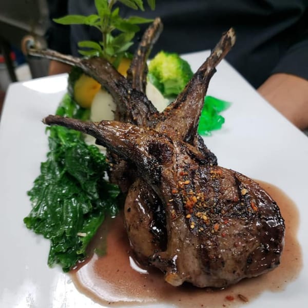 Grilled lamb chops with a side of green vegetables, mashed potatoes, and a sprig of basil.