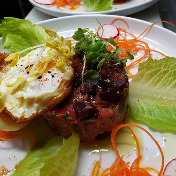 La Brochette Bistro's beef tartare with a fried egg, microgreens, lettuce, and shredded carrots.