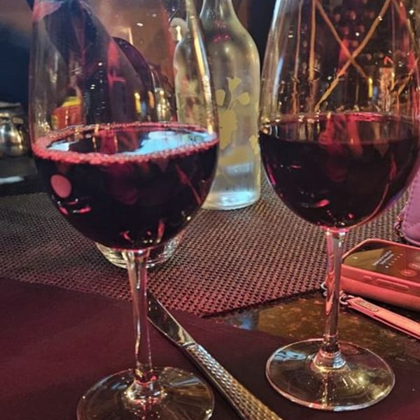 Two glasses of red wine on a table with a water bottle and a phone in the background.
