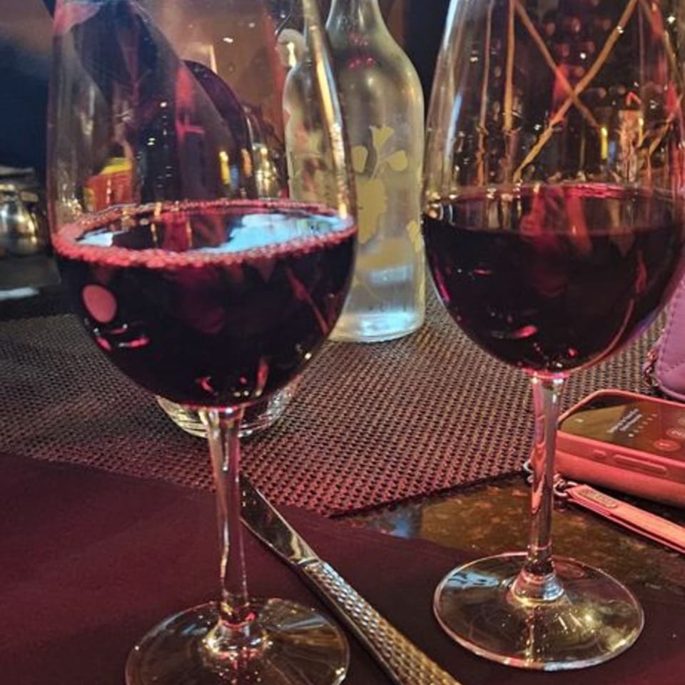 Two glasses of red wine on a table with a water bottle and a phone in the background.
