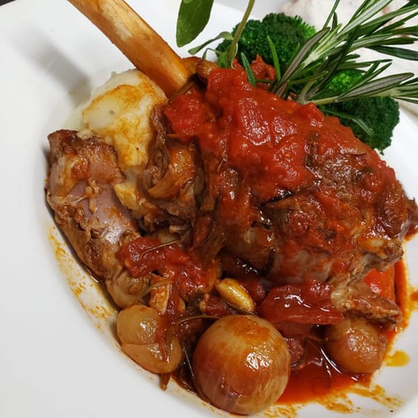 Braised lamb shank with mashed potatoes, tomato sauce, pearl onions, broccoli, and rosemary.