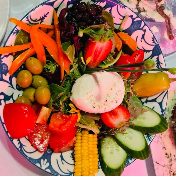 Colorful La Brochette Bistro salad with mozzarella, strawberries, corn, olives, and bell peppers on a patterned plate.