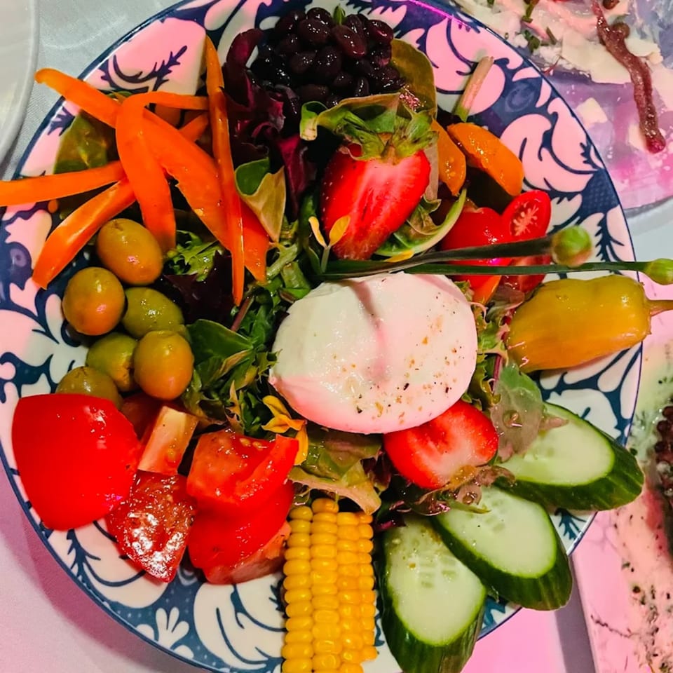 Colorful La Brochette Bistro salad with mozzarella, strawberries, corn, olives, and bell peppers on a patterned plate.