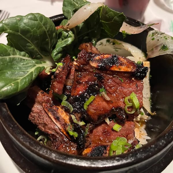 Grilled short ribs with green onions, bok choy, and sliced onions in a dark bowl.