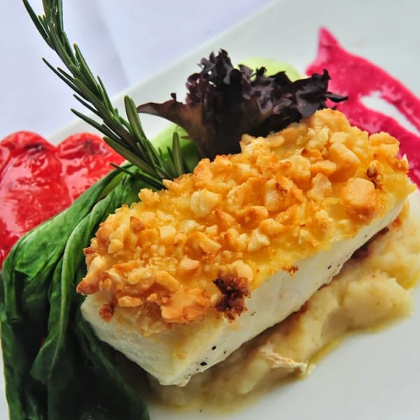Crispy almond-crusted fish over mashed potatoes with red peppers, spinach, and rosemary garnish.