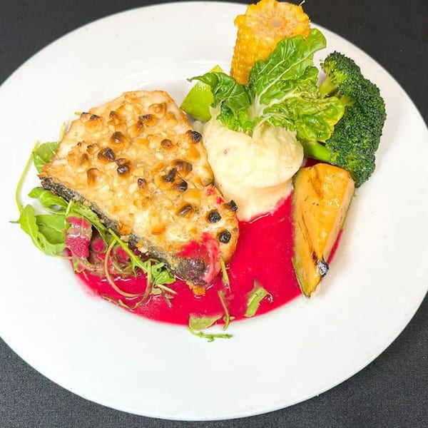 A French dish with fish, mashed potatoes, broccoli, corn, and a vibrant red sauce.