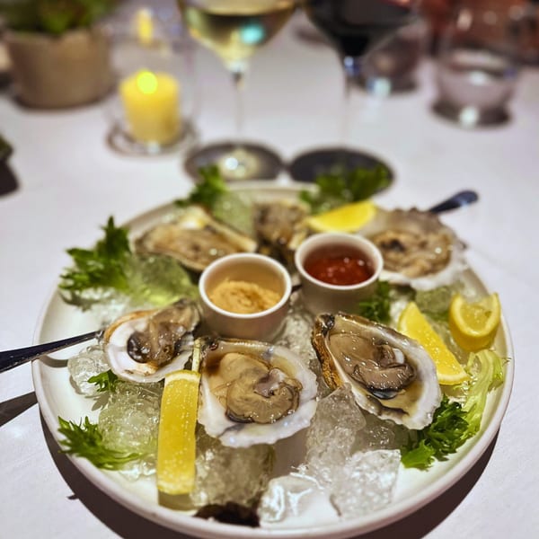 A plate of fresh oysters on ice with lemon wedges and two dipping sauces at La Brochette Bistro.