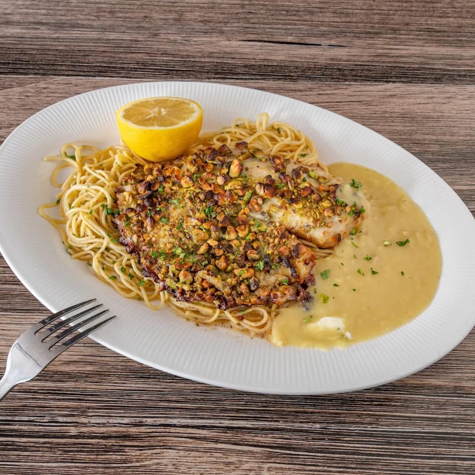 La Brochette Bistro's pistachio-crusted fish with spaghetti, lemon, and creamy sauce on a white plate.
