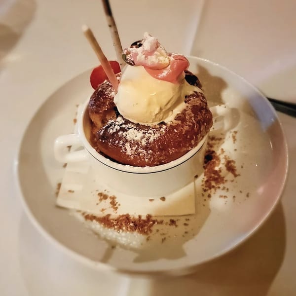 A French dessert with a donut-like pastry, vanilla ice cream, and pink frosting in a white cup.