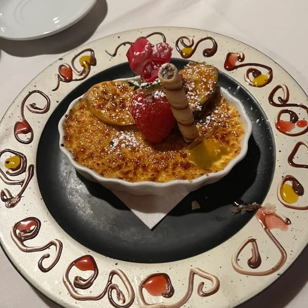 French crème brûlée dessert with strawberries, wafer, and rose petals on a decorative plate.