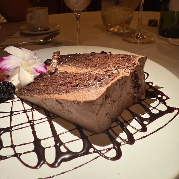 A slice of chocolate cake with whipped cream, berries, and an orchid on a white plate.