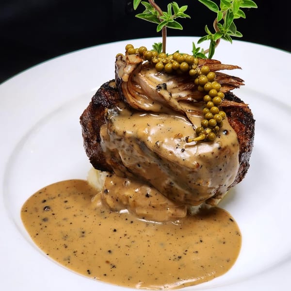 La Brochette Bistro's steak with creamy peppercorn sauce, garnished with green peppercorns and herbs.