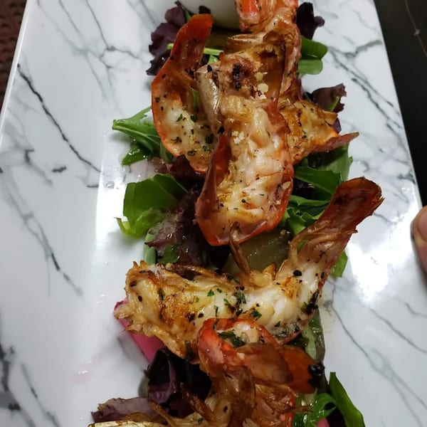 Grilled shrimp with fresh greens and herbs on a white marble plate at La Brochette Bistro.