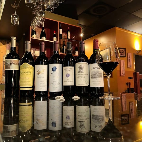 A selection of red wine bottles and a glass of red wine on a bar at La Brochette Bistro.