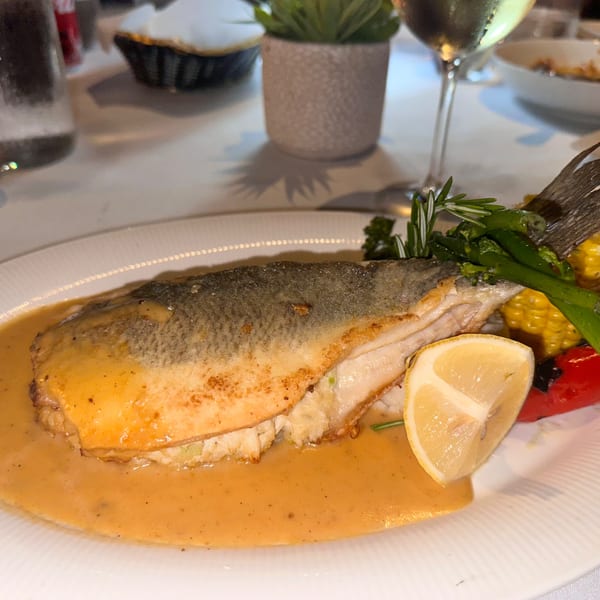Pan-seared fish with sauce, lemon, asparagus, and corn on a white plate at La Brochette Bistro.