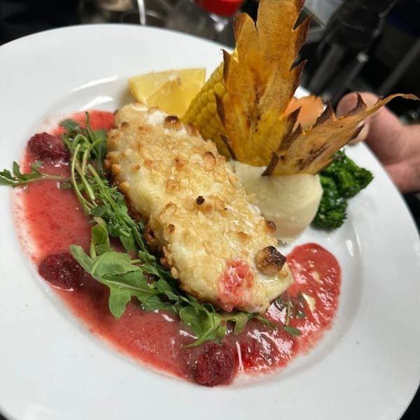 Crispy fish with raspberry sauce, mashed potatoes, corn, broccoli, and lemon on a white plate.