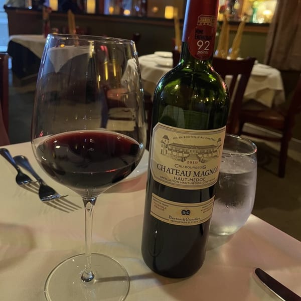 A bottle of Chateau Magnol red wine and a glass of red wine on a white tablecloth.