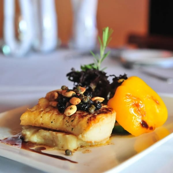 Pan-seared fish with almonds, capers, and dried fruit, served with a roasted yellow pepper.
