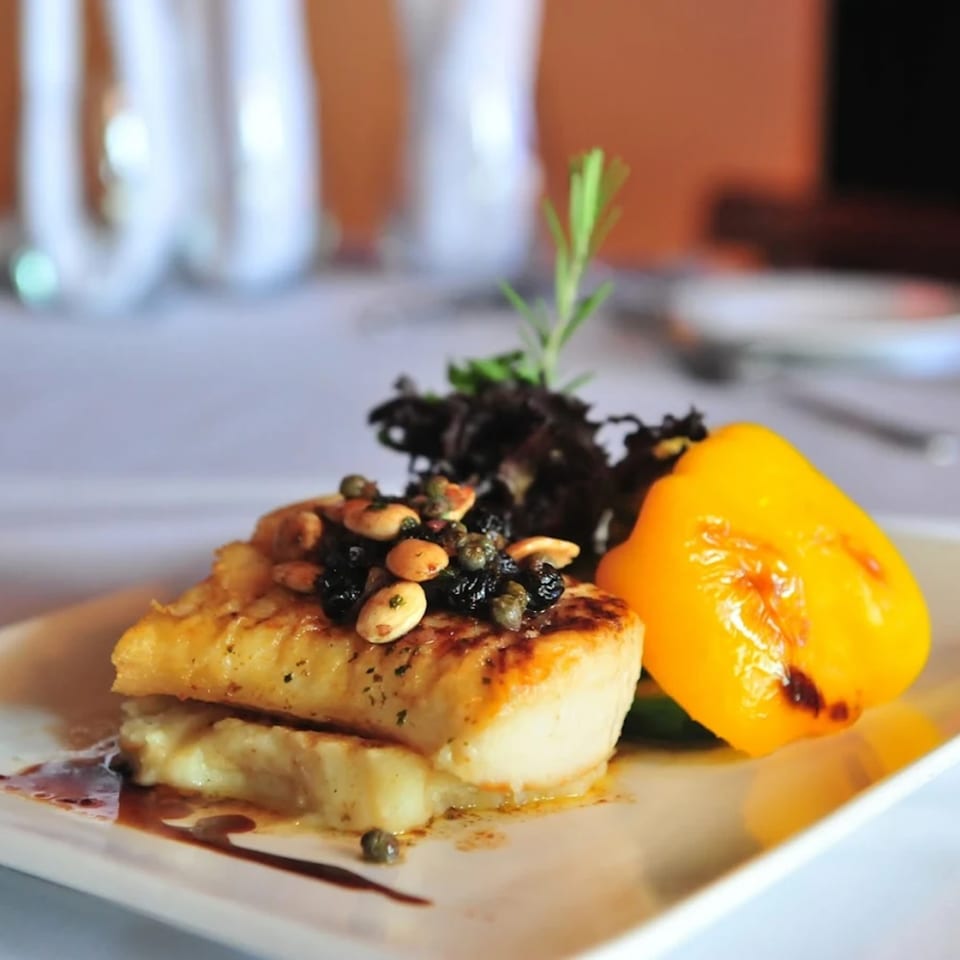 Pan-seared fish with almonds, capers, and dried fruit, served with a roasted yellow pepper.