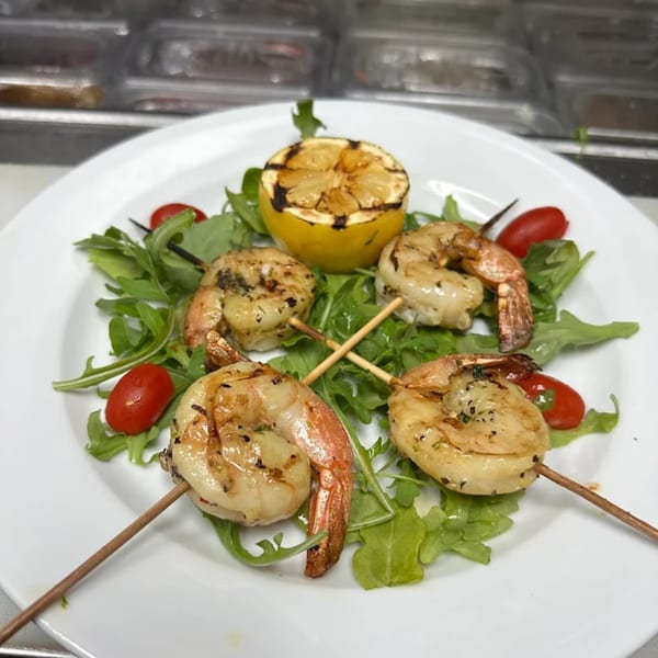 Grilled shrimp skewers with arugula, cherry tomatoes, and a charred lemon half on a white plate.
