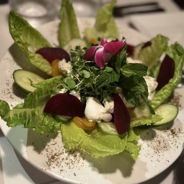 A vibrant La Brochette Bistro salad with lettuce, beets, cucumbers, cheese, and a pink edible flower.