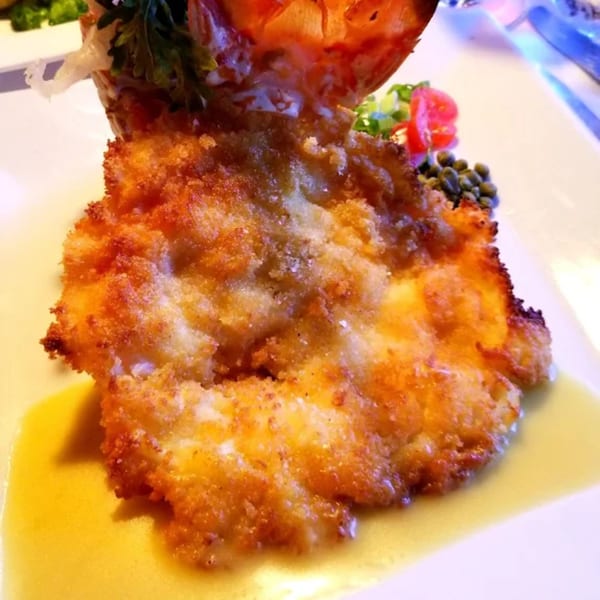 Golden-fried chicken cutlet with a side of capers, cherry tomatoes, and greens at La Brochette Bistro.