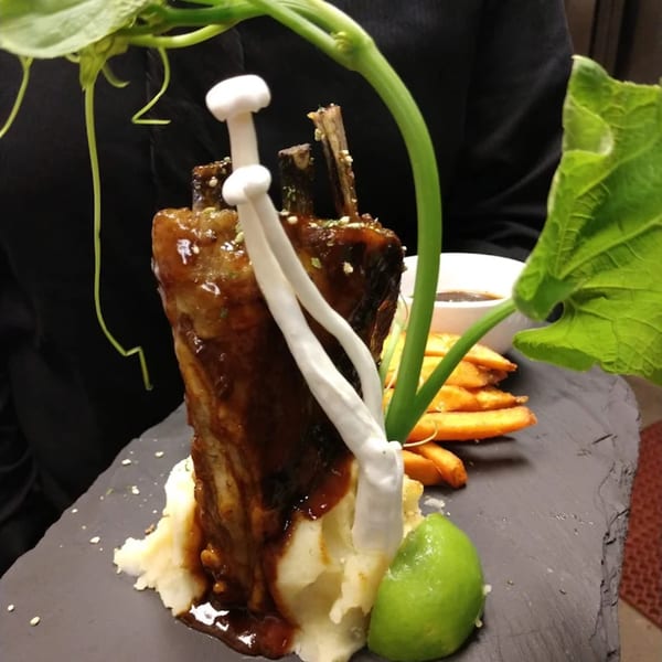 Glazed ribs on mashed potatoes with fries, mushrooms, and a lime wedge on a slate plate.