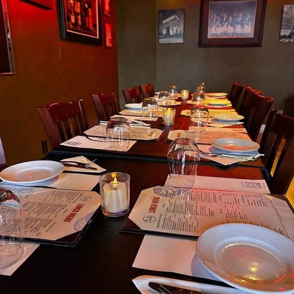 A long dining table set with plates, glasses, menus, and candles in a French bistro.