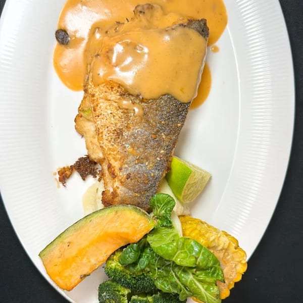 Pan-seared fish with creamy sauce, broccoli, corn, and a slice of melon on a white plate.