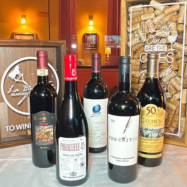 Five bottles of red wine, including "The Critic" and "Caymus Vineyards," displayed on a table.