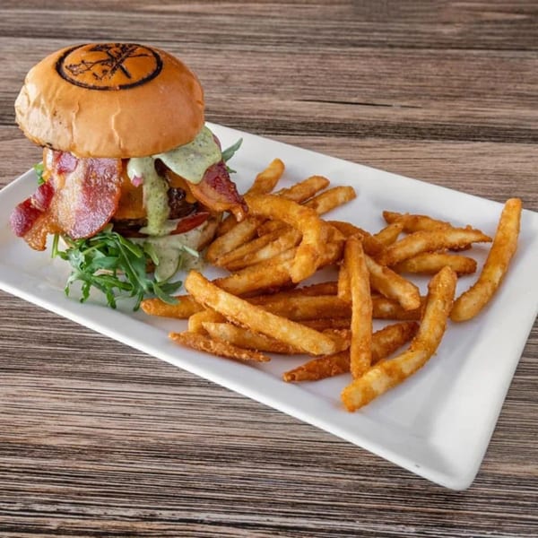La Brochette Bistro's burger with bacon, green sauce, and arugula, served with golden fries.