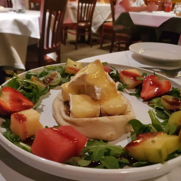 Baked brie with honey, fruit, and arugula on a white plate at La Brochette Bistro.