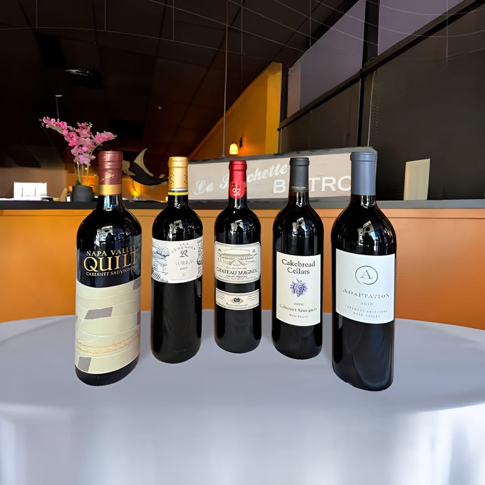 Five bottles of red wine on a white tablecloth, with the "La Brochette Bistro" sign in the background.